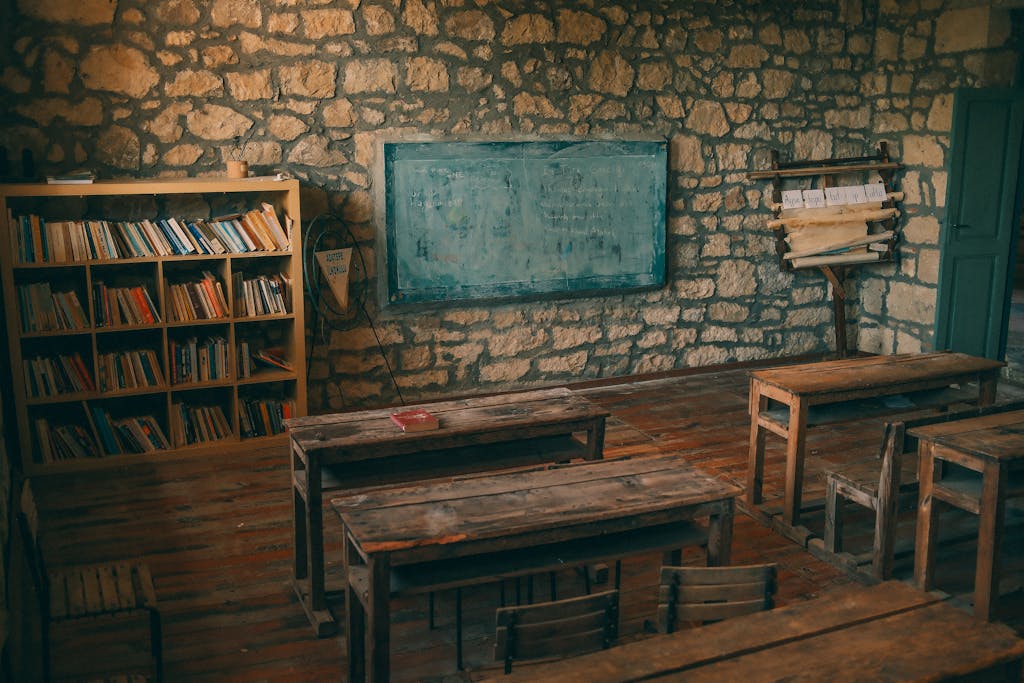 An empty rustic classroom featuring stone walls, wooden desks, and a chalkboard, evoking a sense of nostalgia.